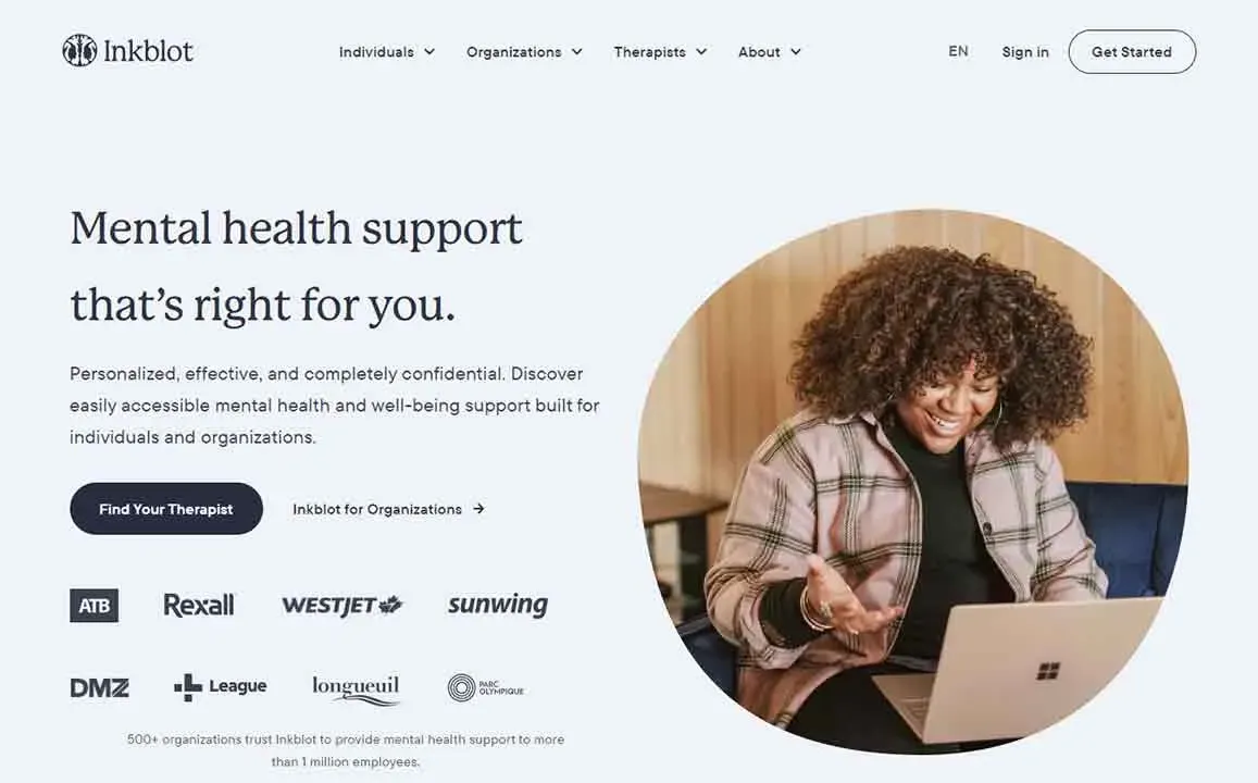 A person with curly hair smiles while using a laptop in a cozy room, highlighting engaging online mental health support services.