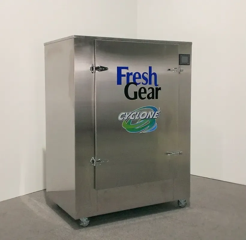 Una máquina Fresh Gear Cyclone de acero inoxidable se encuentra sobre un piso alfombrado, con un diseño elegante y rectangular con ruedas para movilidad, y una pantalla digital en la puerta para control, ideal para procesos de saneamiento y desinfección industrial.
