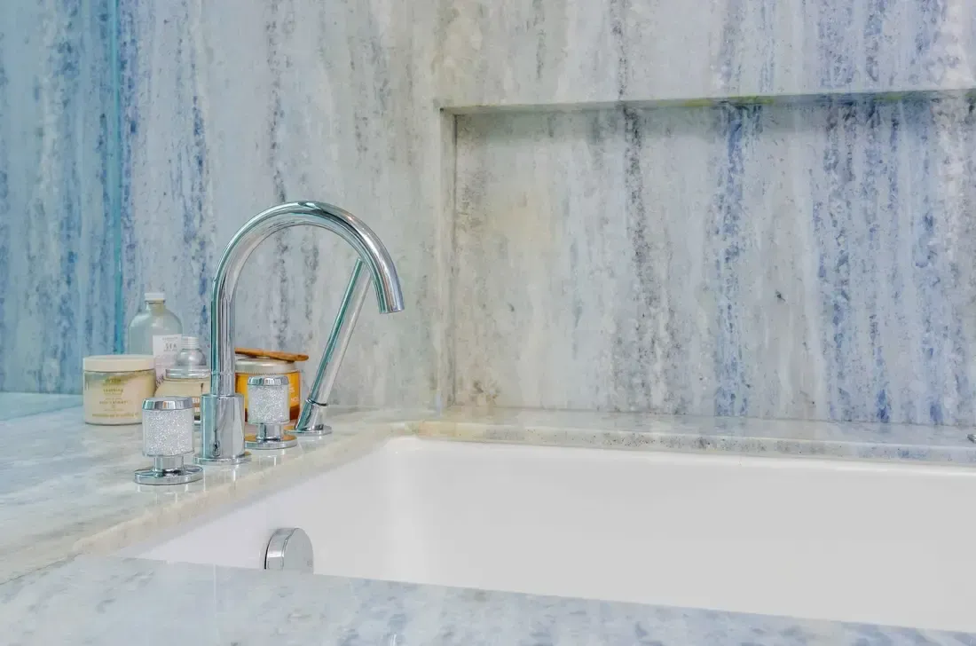 Baño de mármol lujoso con un grifo plateado elegante y artículos de tocador dispuestos ordenadamente en el mostrador, ejemplificando un diseño interior elegante.