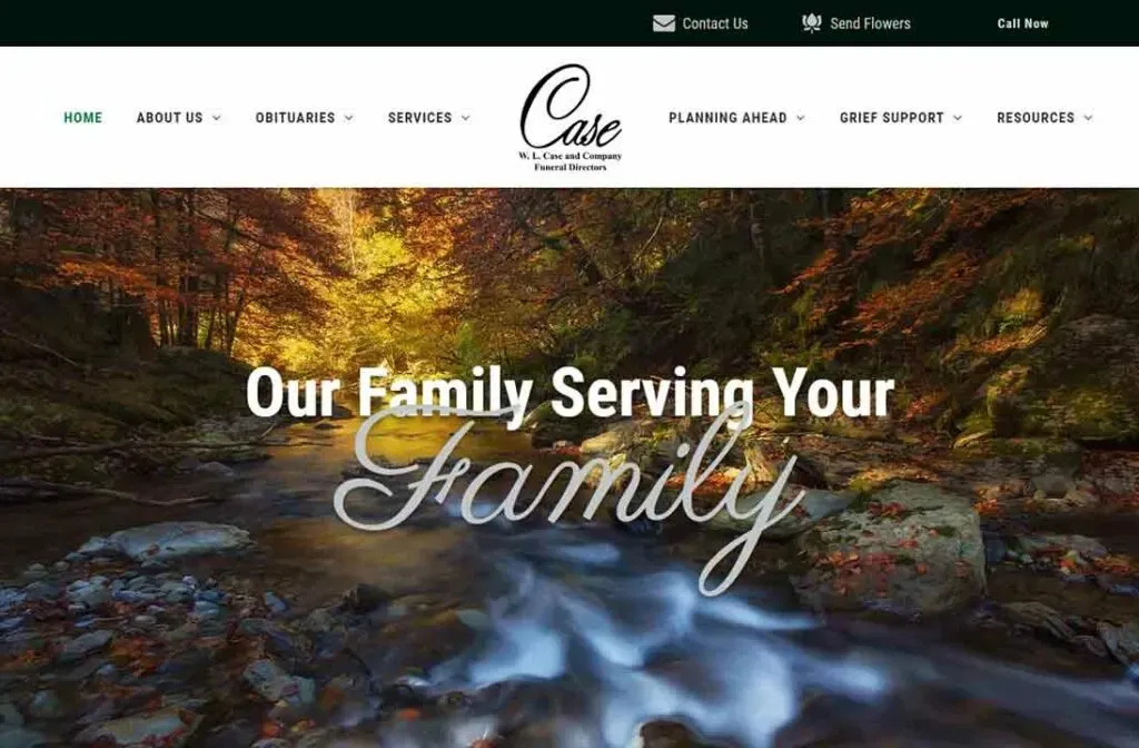 A serene forest scene with a flowing stream surrounded by vibrant autumn foliage, overlaid with text that reads "Our Family Serving Your Family", promoting a funeral service company's compassionate care and support amidst nature's tranquility.