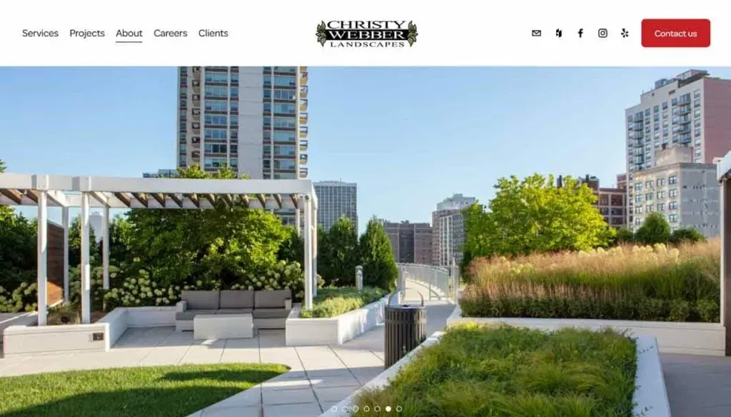 A modern urban rooftop garden features lush green plants, a white pergola with seating, and city skyscrapers in the background under a clear blue sky, highlighting sustainable landscape design.