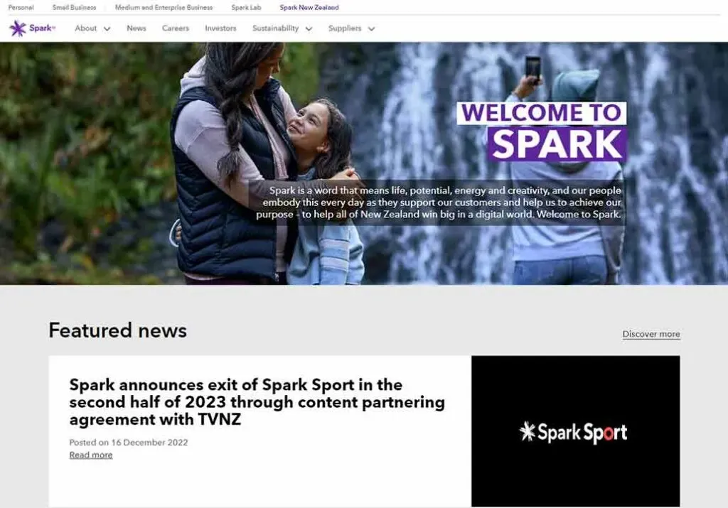 A person in outdoor attire holds a child in a scenic location with a cascading waterfall backdrop, accompanied by the text "Welcome to Spark," highlighting a digital world commitment in New Zealand.