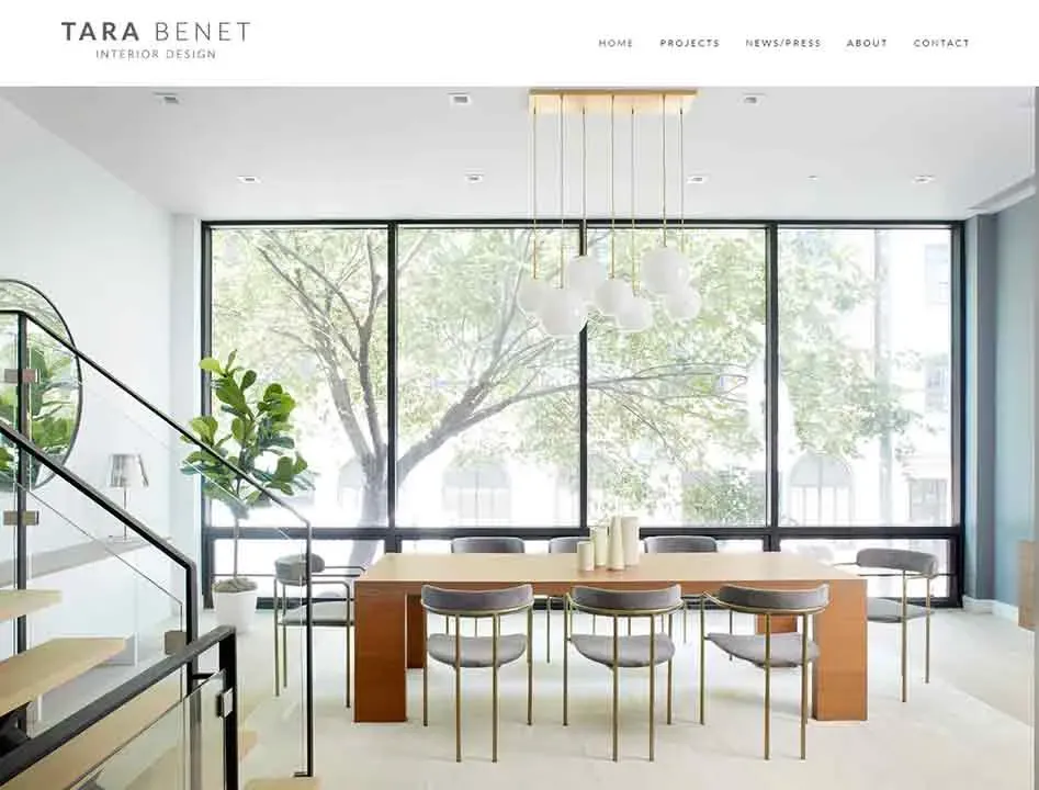 Modern dining room with a large wooden table and sleek gray chairs, featuring a minimalist chandelier and expansive floor-to-ceiling windows offering a lush view of outdoor trees, in a sophisticated interior design setting.