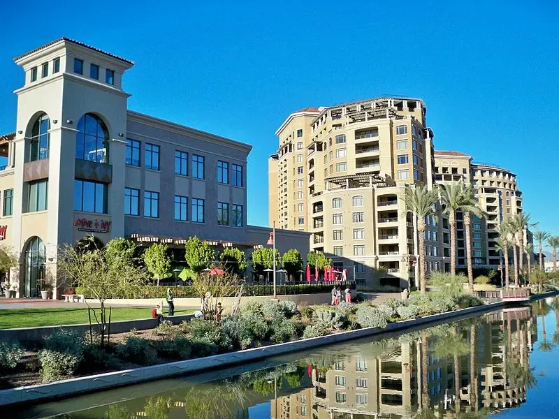 Imagen del Scottsdale Waterfront mostrando edificios modernos con balcones, vegetación exuberante y un canal claro que refleja la vibrante arquitectura contra un cielo azul brillante.