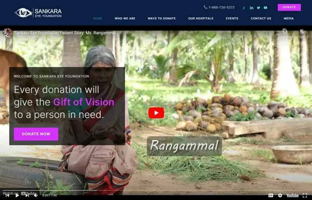 A senior woman with long hair sits on a stone bench in a lush garden surrounded by coconut trees, highlighted by text overlay encouraging donations to the Sankara Eye Foundation for providing the gift of vision.