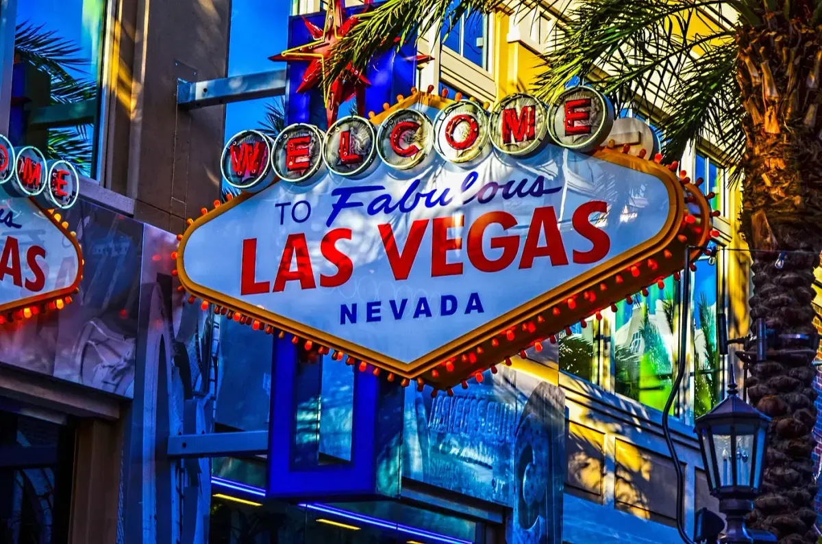 El icónico letrero "Welcome to Fabulous Las Vegas, Nevada" está brillantemente iluminado bajo palmeras con vibrantes luces de neón, reflejando el ambiente bullicioso y energético del Strip de Las Vegas.