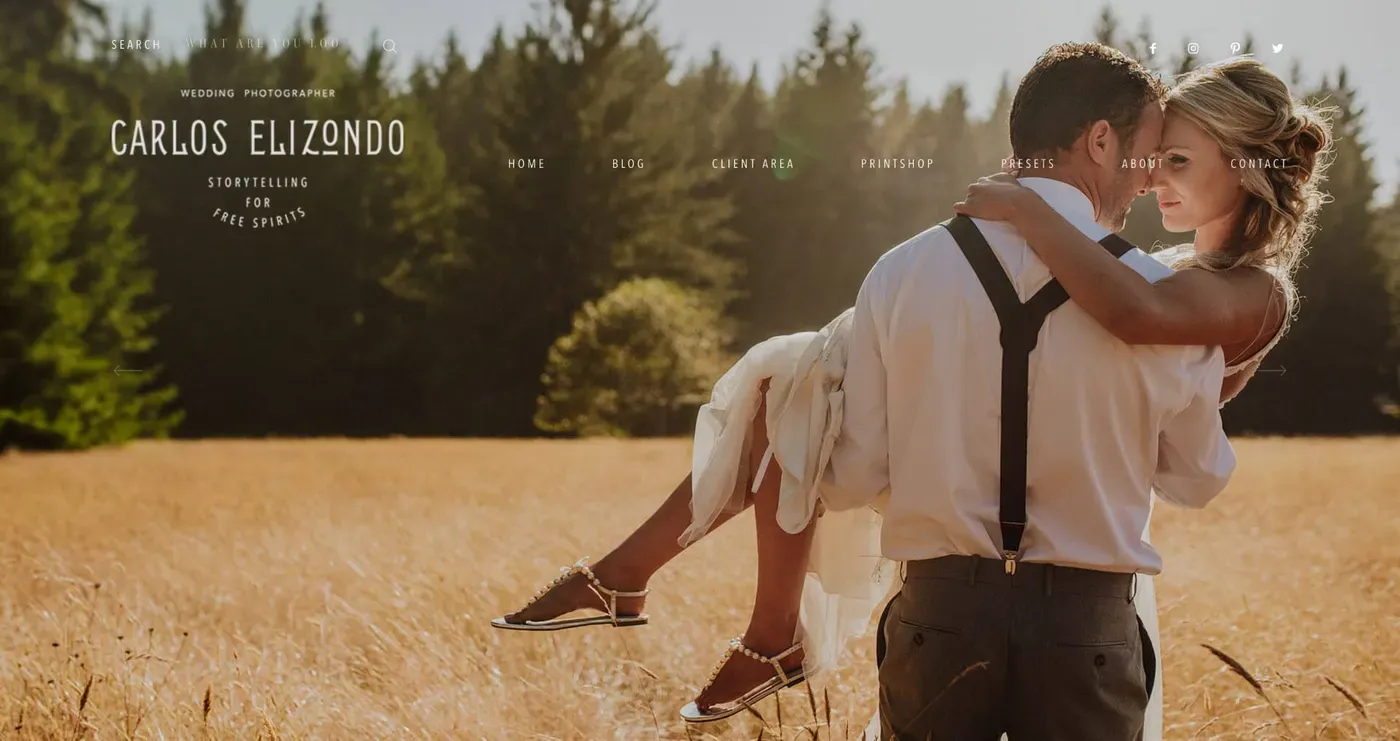 A groom carries his bride through a golden wheat field under a clear sky, surrounded by lush greenery, capturing a romantic wedding moment.