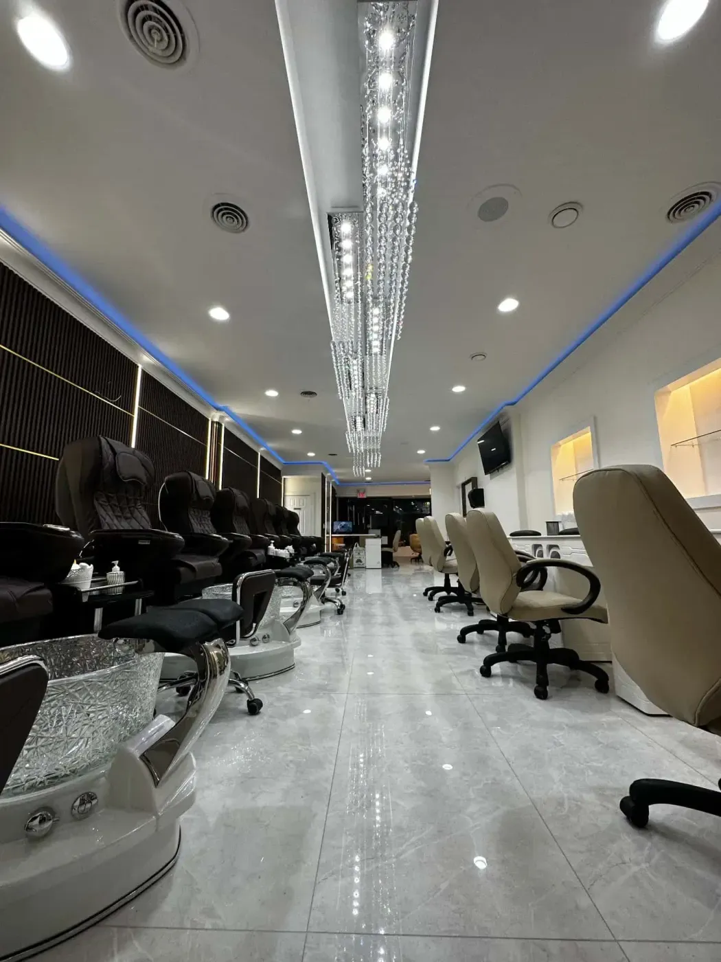Un interior moderno y lujoso de salón de uñas con sillas de pedicura elegantes y cómodas con baños de pies, sillas giratorias con estilo, un piso de baldosas pulido y una iluminación ambiental con accesorios decorativos en el techo.