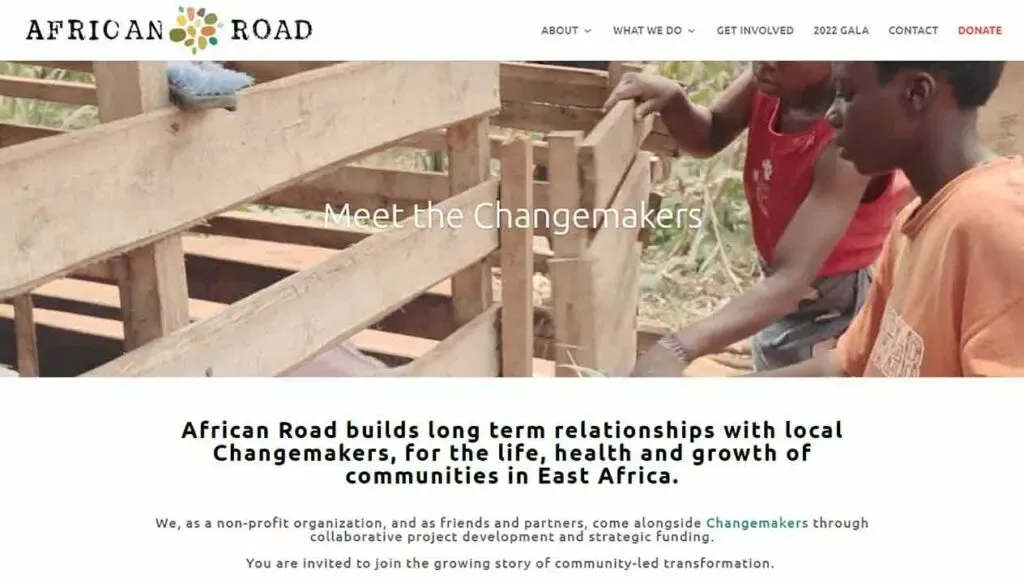 The image shows a website banner featuring two individuals constructing a wooden structure, with the text "Meet the Changemakers" overlaid, promoting African Road's mission to build community relationships in East Africa.