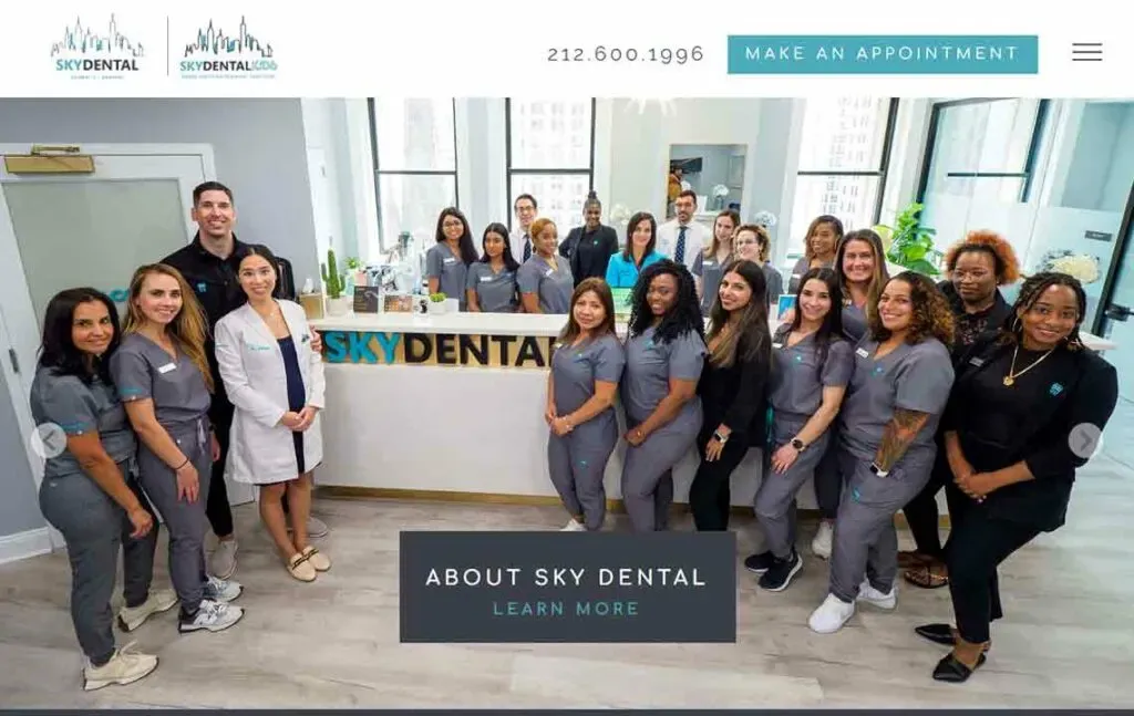 A diverse dental team, dressed in uniforms, poses together behind the front desk at a modern dental clinic called Sky Dental, with a bright and welcoming interior.