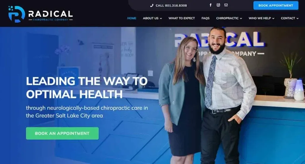A man and a woman stand smiling at a reception desk in a modern chiropractic clinic, with a booking button and slogan promoting chiropractic care in the Greater Salt Lake City area visible on the wall.