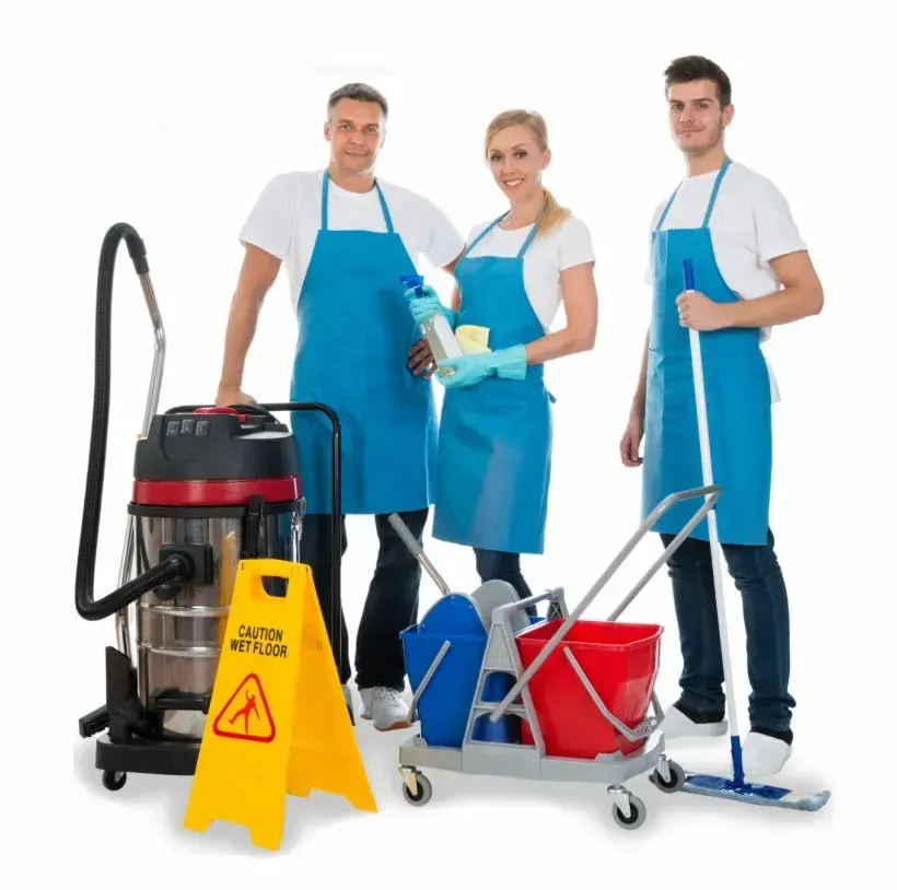 Tres empleados de limpieza con delantales azules sonríen con suministros de limpieza, junto a una aspiradora, trapeador, cubetas y un letrero de "Cuidado Piso Mojado".