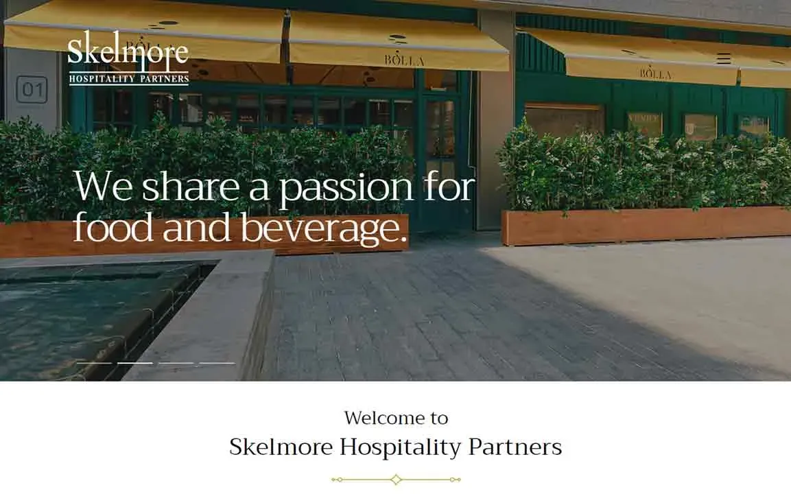 The image shows the exterior of a restaurant with a yellow awning and a row of lush greenery in planter boxes, featuring the Skelmore Hospitality Partners logo and the text "We share a passion for food and beverage."