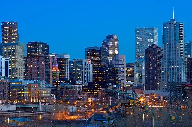 Horizonte de una vibrante ciudad al anochecer mostrando rascacielos iluminados contra un cielo azul claro, destacando una mezcla de estilos arquitectónicos y una vida urbana bulliciosa.