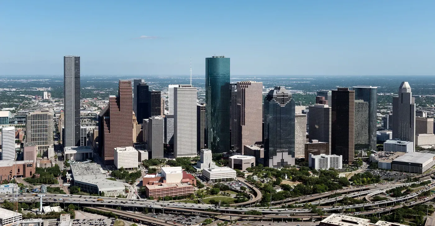 Vista aérea de un paisaje urbano bullicioso que muestra el icónico horizonte de Houston, con una mezcla de rascacielos modernos y monumentos arquitectónicos bajo un cielo azul claro.