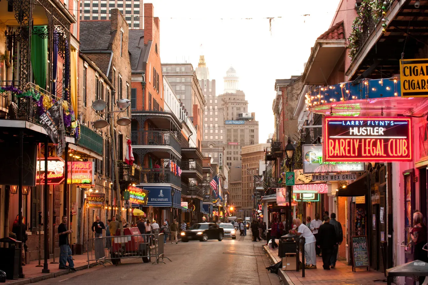 A vibrant evening scene on Bourbon Street in New Orleans, featuring colorful neon signs, historic buildings, and bustling pedestrian activity with festive decorations, capturing the lively atmosphere of the French Quarter.