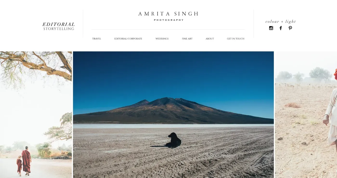 A lone figure in dark clothing sits on a vast, barren salt flat with a towering, mountainous landscape under a clear blue sky in the background.