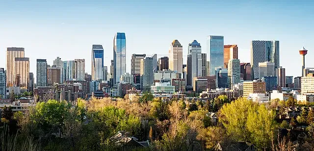 Vista panorámica del horizonte de Calgary con modernos rascacielos y edificios de oficinas enmarcados por exuberante vegetación bajo un cielo azul claro.