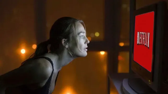 Mujer inclinándose cerca de una pantalla de TV que muestra el logo rojo de Netflix en una habitación oscura